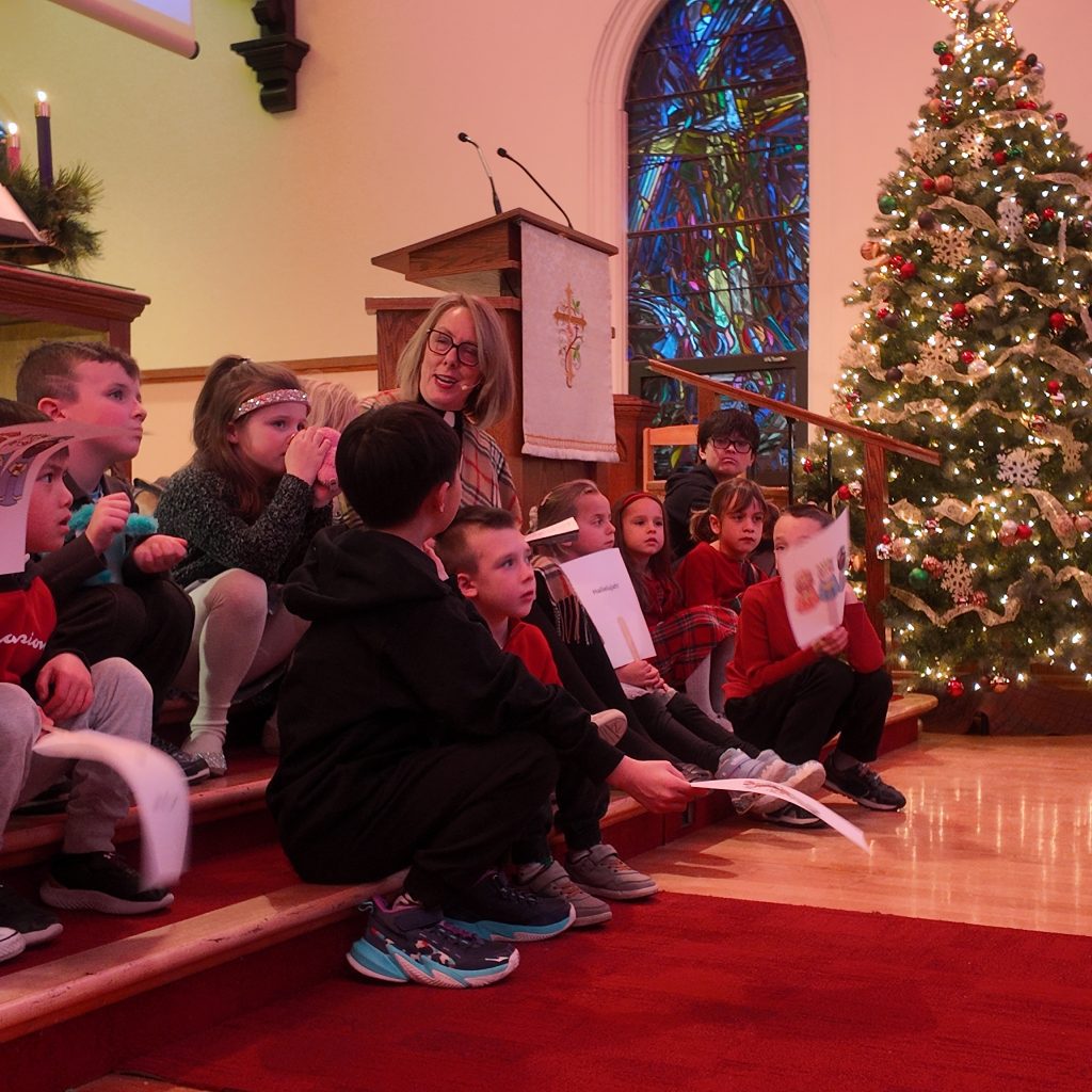 Rev Lori is sharing a Christmas story with all the kids on the steps in front of the pulpit.
