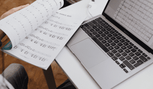 A music scoresheet is opened in front of the laptop